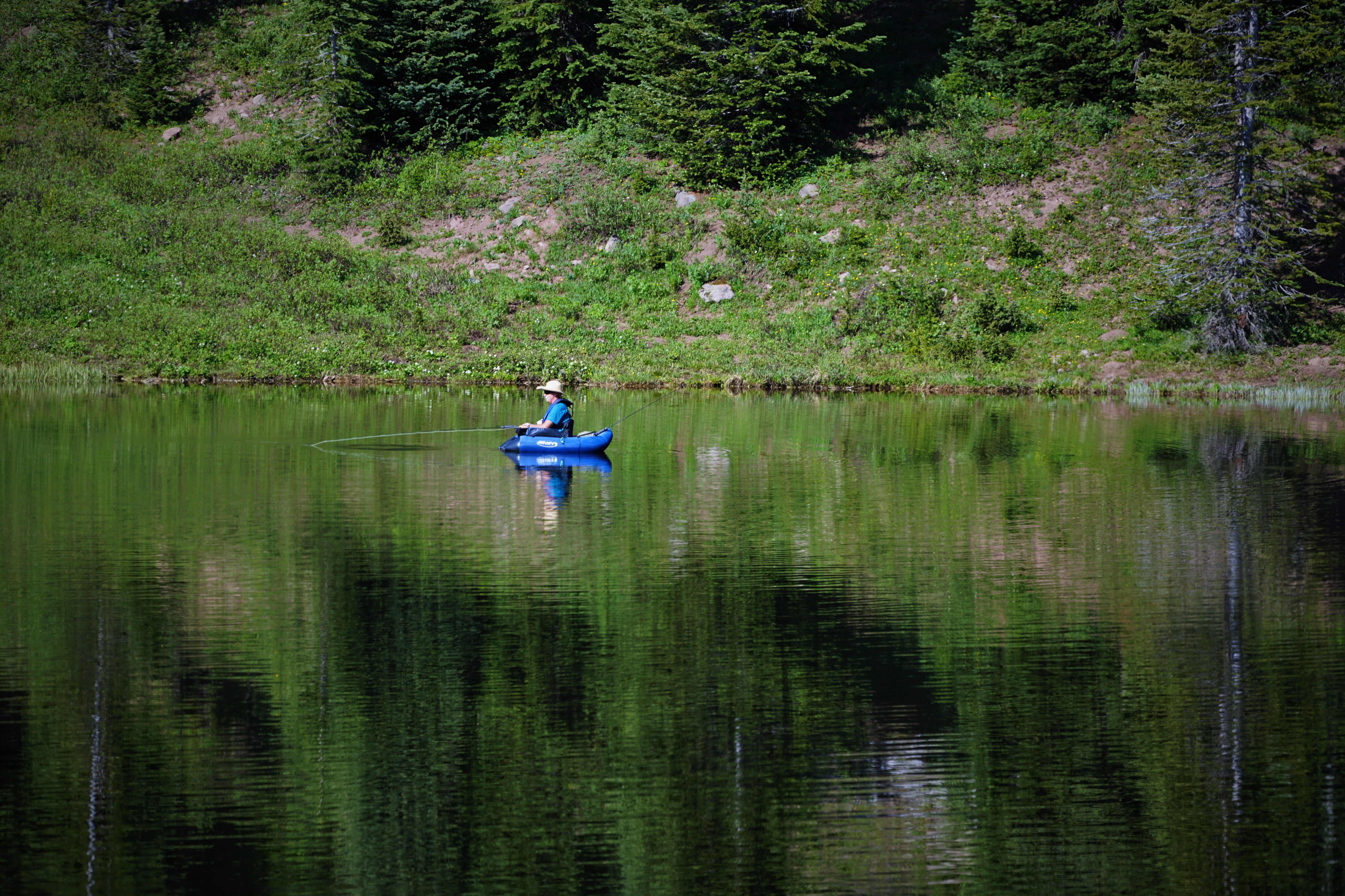 man fishing in mountain lake in blue inner tube boat