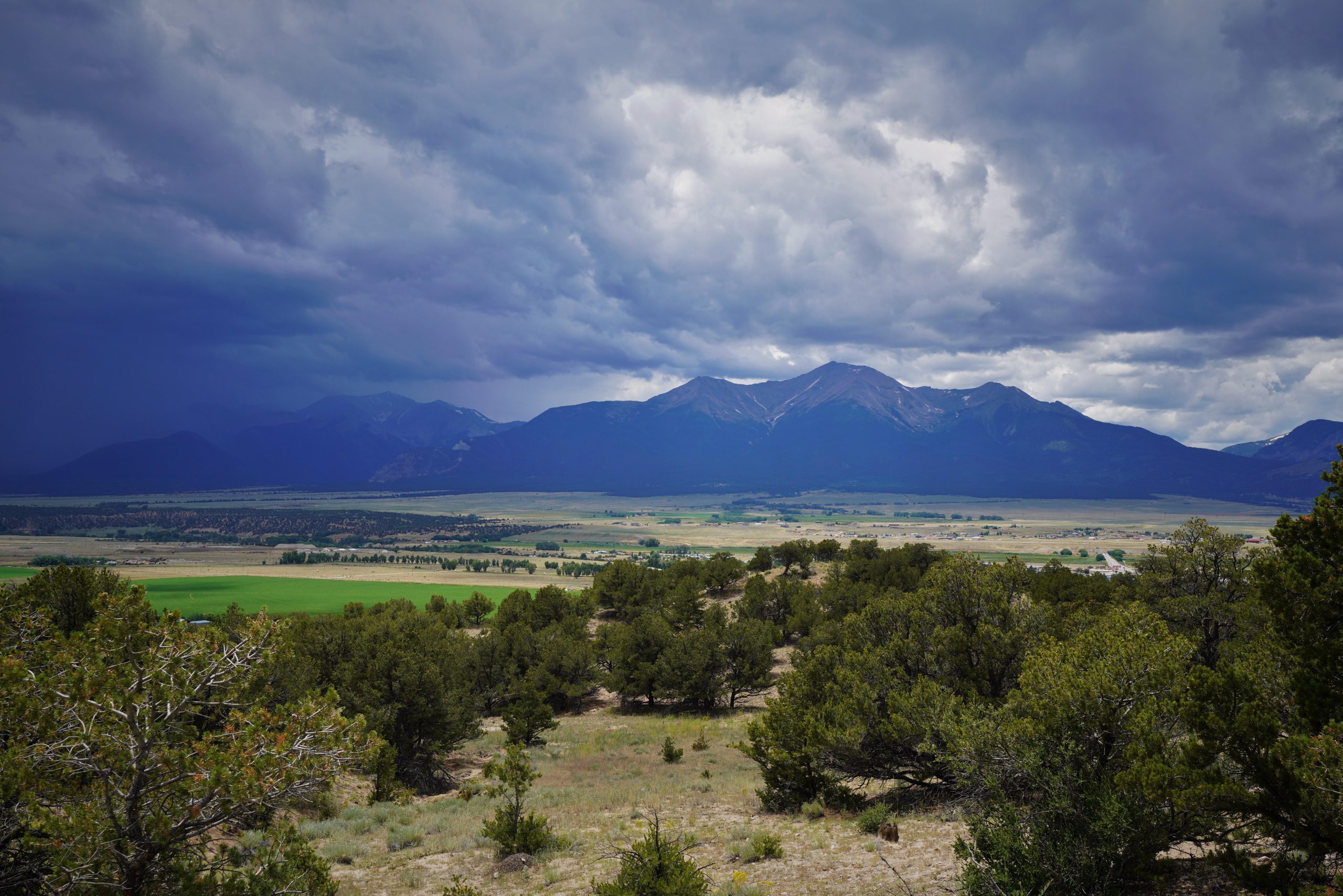 view of the Collegiate Peaks mountain range with green fields in the foreground and cloudy skies